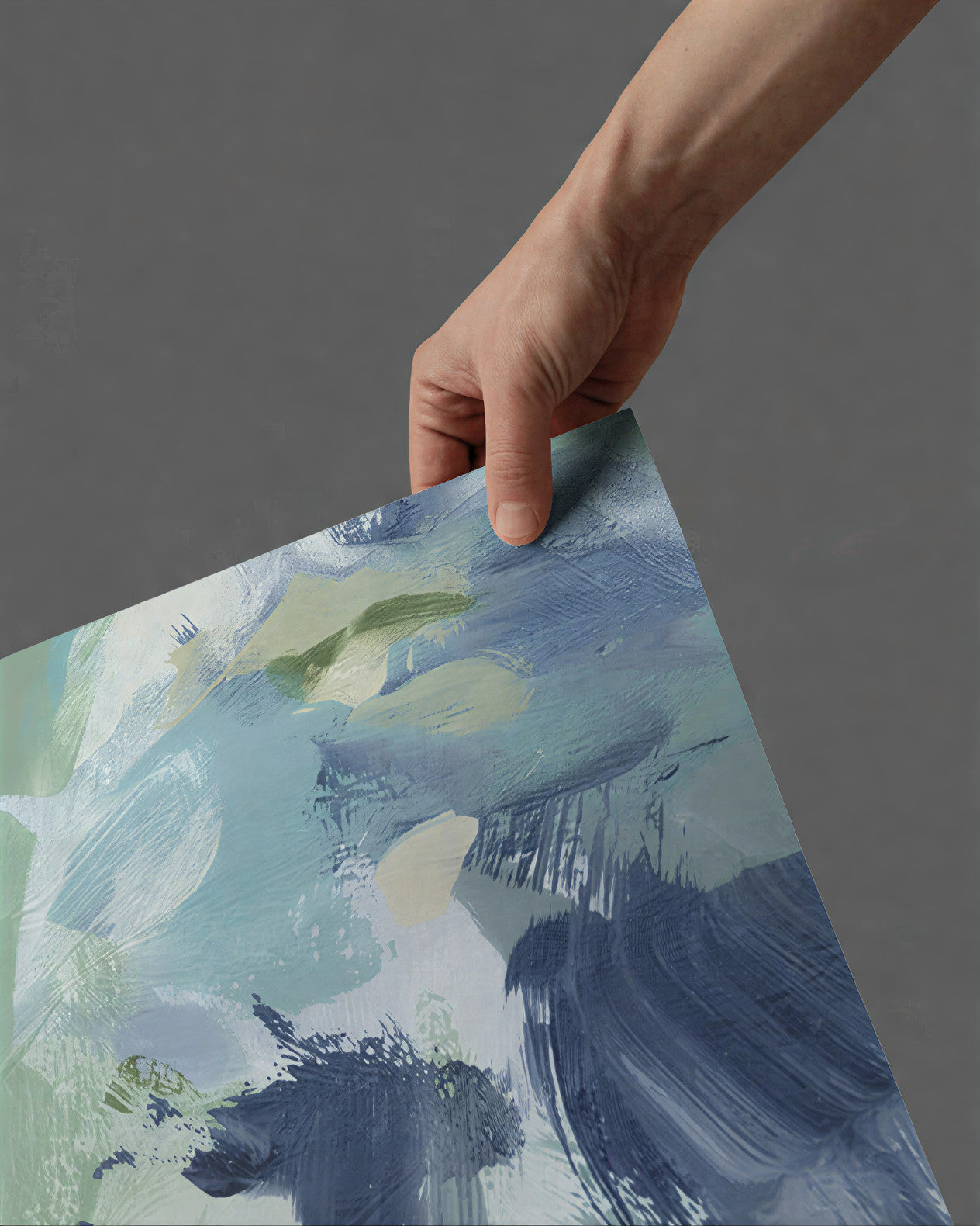 Hand holding a piece of abstract art with blue and green brush strokes on a gray background