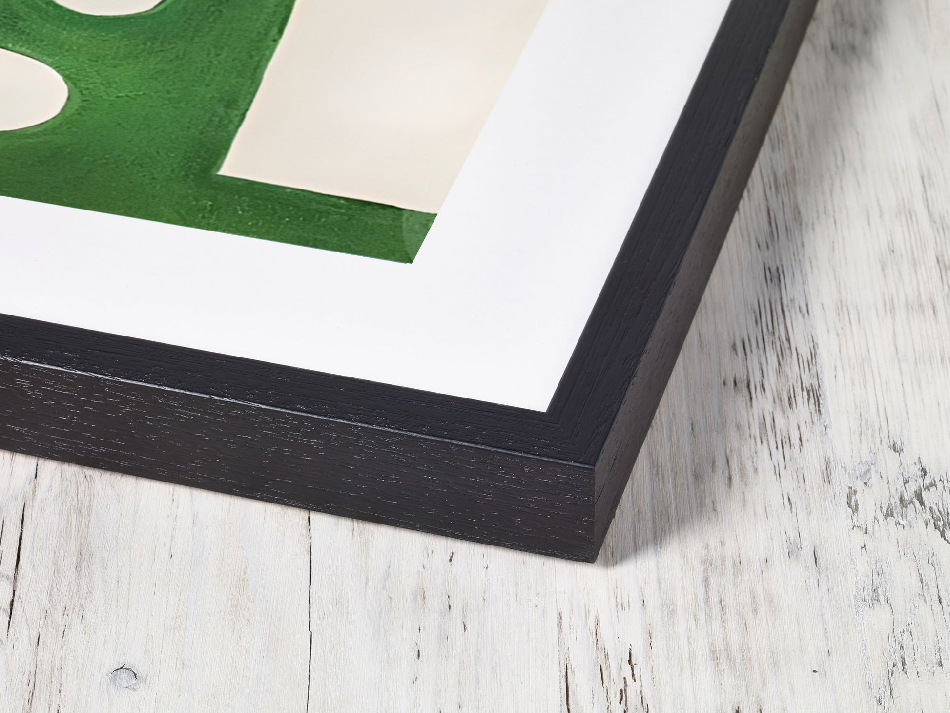 Framed artwork with a green abstract design on a white background, placed on a wooden surface.