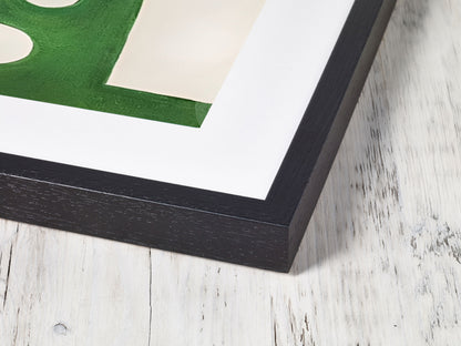 Framed artwork with a green abstract design on a white background, placed on a wooden surface.