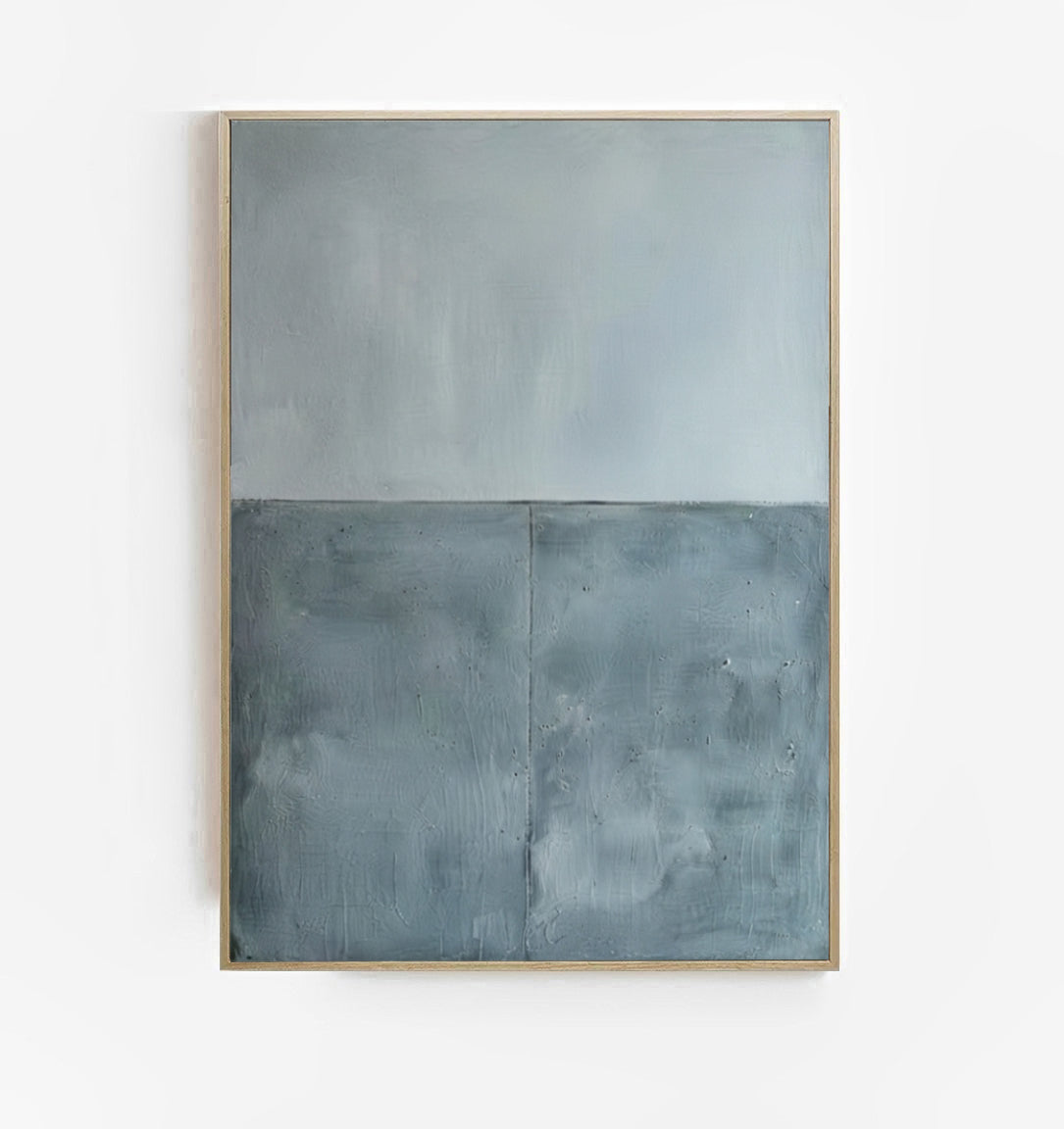 An Large Textured Blue and Gray Abstract Canvas Art featuring a horizontal split design with a light gray textured top half and a darker slate blue textured bottom half, enclosed in a thin light wood frame and mounted on a white wall.