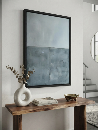 Framed Neutral blue gray textured wall art for Scandinavian and contemporary interiors by Noho Art Gallery with a black frame hangs on a white wall above a rustic wooden console table. The artwork features a textured, two-tone design in shades of slate blue and gray.