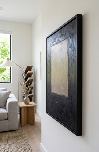 A large framed abstract wall art print hangs on a white wall in a modern living room setting. The artwork features a textured black border with a central beige and gray panel.