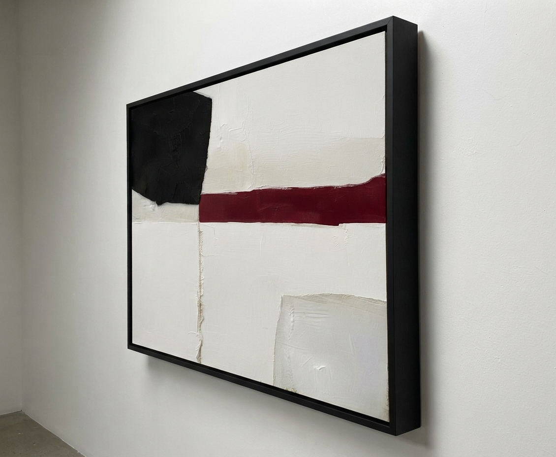 A framed Minimalist black and white abstract canvas with red accent, hand-painted textured abstract canvas by Noho Art Gallery hanging on a white wall. The artwork features a large black block, a horizontal dark red stripe, and textured off-white sections, enclosed in a slim black frame.