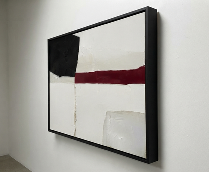 A framed Minimalist black and white abstract canvas with red accent, hand-painted textured abstract canvas by Noho Art Gallery hanging on a white wall. The artwork features a large black block, a horizontal dark red stripe, and textured off-white sections, enclosed in a slim black frame.