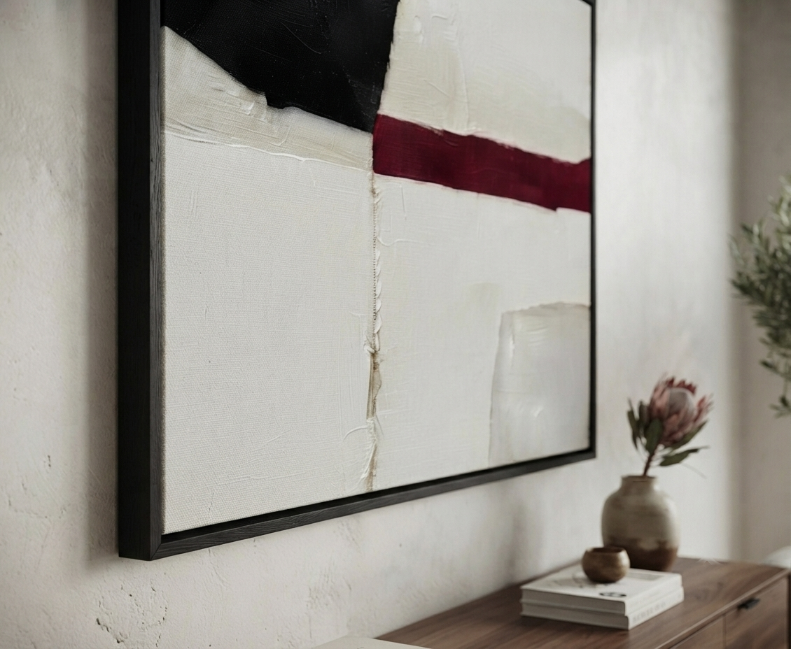 A Minimalist black and white abstract canvas with red accent, buy original contemporary abstract art for living room by Noho Art Gallery hanging on a textured off-white wall above a wooden console table. The artwork features thick textured brushstrokes in black, off-white, and deep burgundy red.