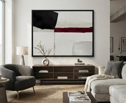 A large Minimalist black and white abstract canvas with red accent, large black and white textured painting with red highlight by Noho Art Gallery hangs above a dark wood console in a modern living room. The artwork features a white background with a bold black block, a horizontal dark red stripe, and soft gray brushstrokes.
