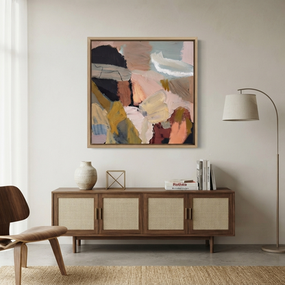 Framed earthy neutral abstract wall art, large textured abstract canvas art, buy unique abstract textured painting, abstract art with earth tones hanging above a wooden sideboard in a modern living room, with a floor lamp, chair, books, and decorative vase visible y Noho Art Gallery.