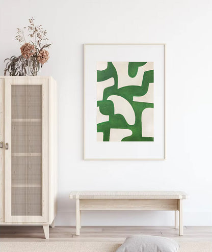 Framed abstract art with green design on a white wall above a wooden bench.