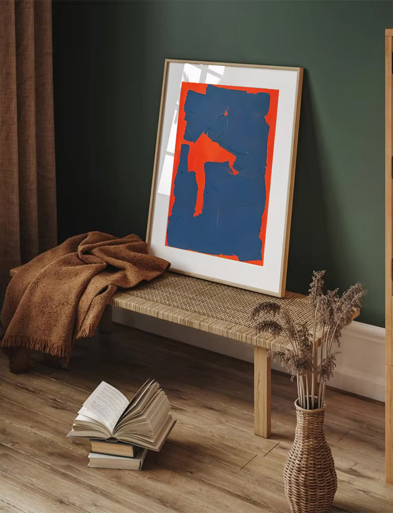 Abstract art print on a wall with a bench, books, and a vase in a room.