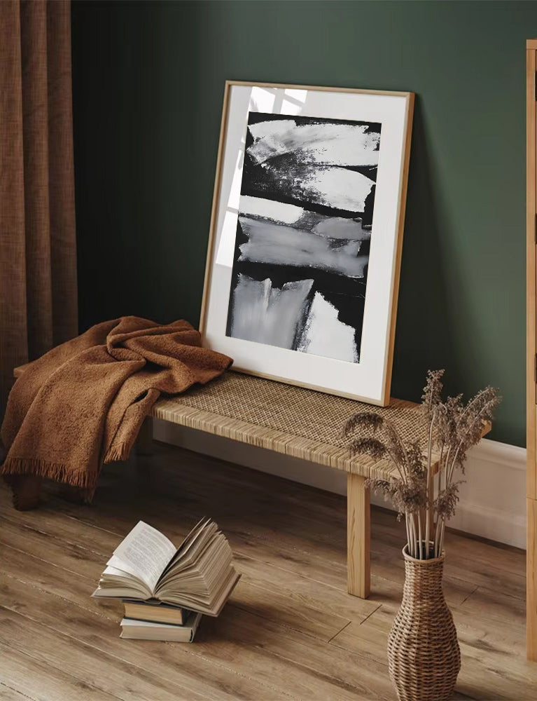 Framed artwork on a wooden bench with books and a vase in a room with green walls.