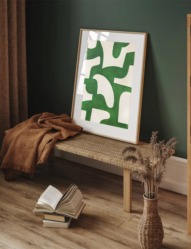Framed abstract art with green shapes on a bench against a dark wall.