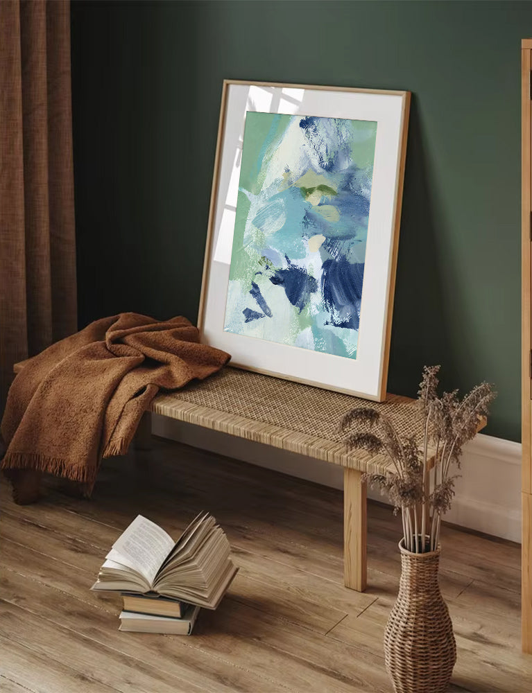 Framed abstract art on a bench with books and a vase in a room.