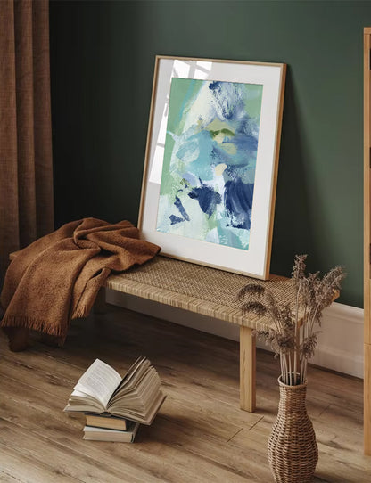 Framed abstract art on a bench with books and a vase in a room.
